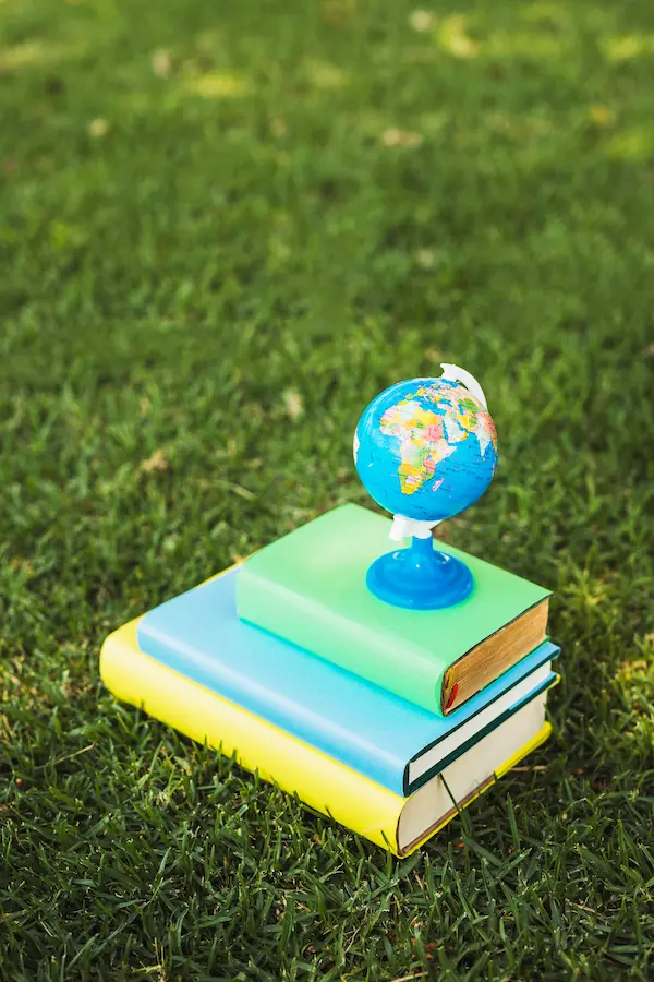 Pequeño globo terráqueo sobre una pila de libros de colores en el césped, contenidos del curso de sostenibilidad y ODS