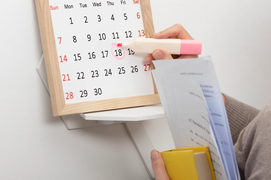 Persona marcando una fecha en un calendario junto a documentos de trabajo